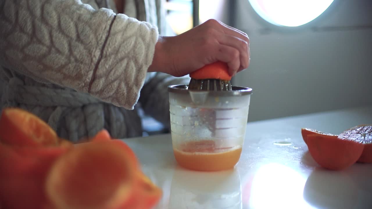 Mujer usando un exprimidor de naranjas, preparando un zumo de naranja en casa.