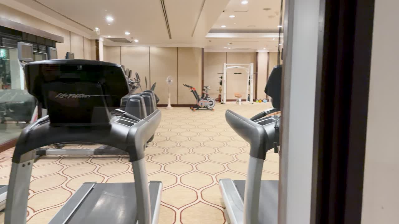 Wide-angle pan across modern hotel fitness center, showing treadmills, gym equipment, and bright lighting