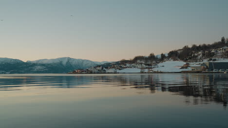 view of ytre samlafjorden in norway, featuring clear waters, snowy mountains across the water, and homes nestled in the winter snow