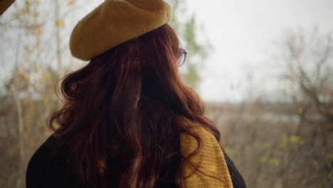 close-up head view of a lady with red wavy hair in sunglasses, looking excited and enjoying nature, using her muffler to cover her mouth as she bends slightly