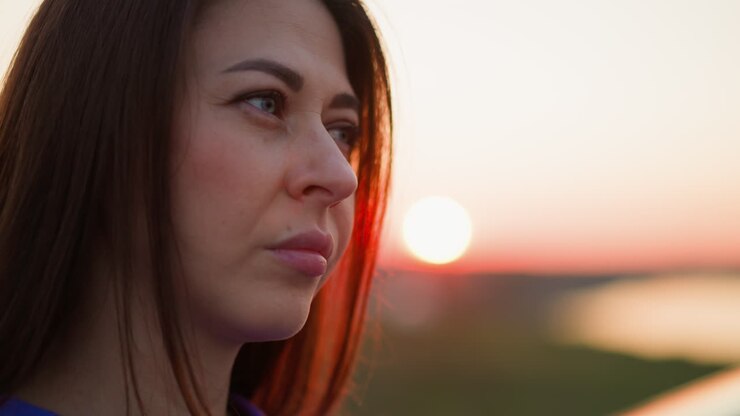 Mujer molesta de pie contra el sol rojo del atardecer, de cerca. Dama de cabello oscuro pensando en las dificultades de la vida.
