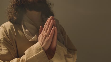 studio portrait of man wearing robes with long hair and beard representing figure of jesus christ praying 1