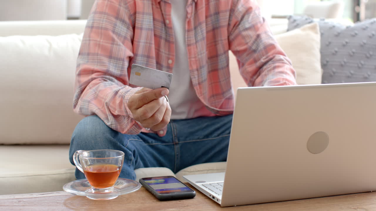 Holding credit card and using laptop, man shopping online at home