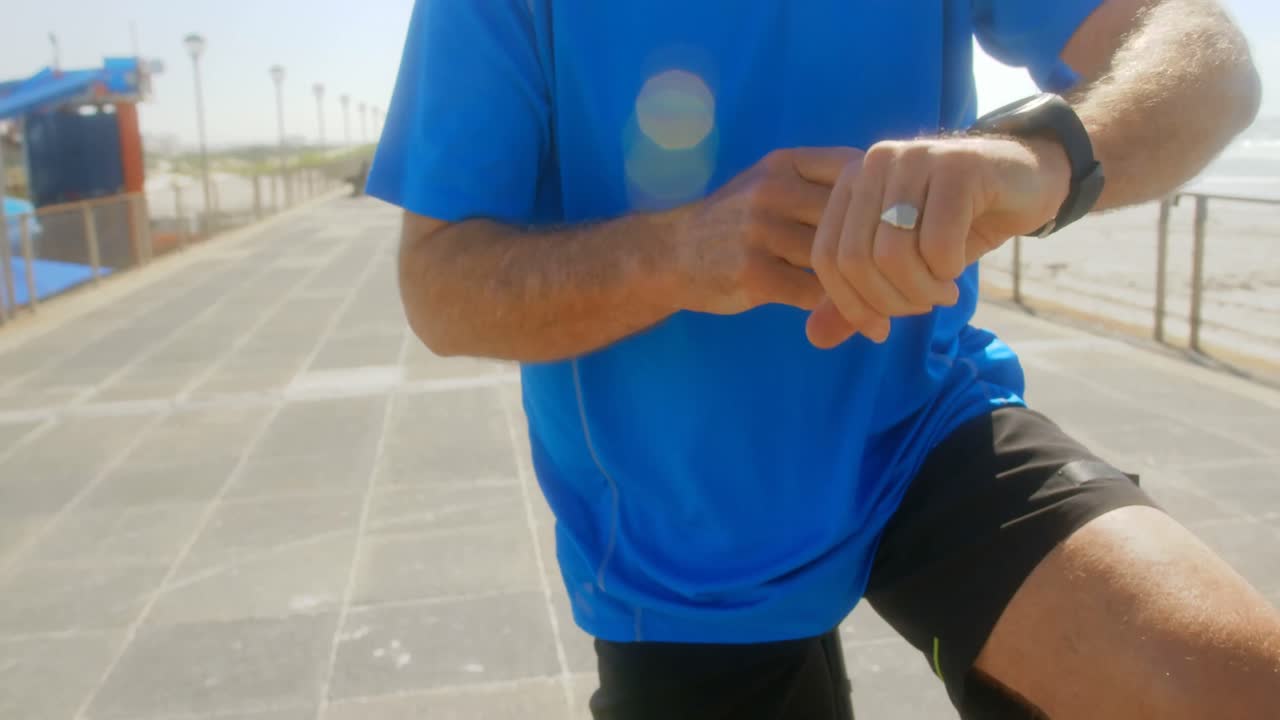 Mid section of active senior man checking time on smartwatch on a promenade at beach 4k