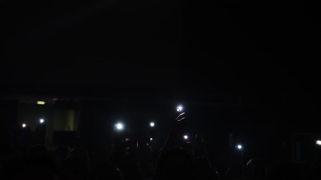 Concert crowd capturing musical moment, smartphone flashlights creating luminous atmosphere with synchronized energy and shared excitement