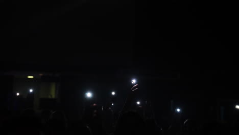 concert crowd capturing musical moment, smartphone flashlights creating luminous atmosphere with synchronized energy and shared excitement