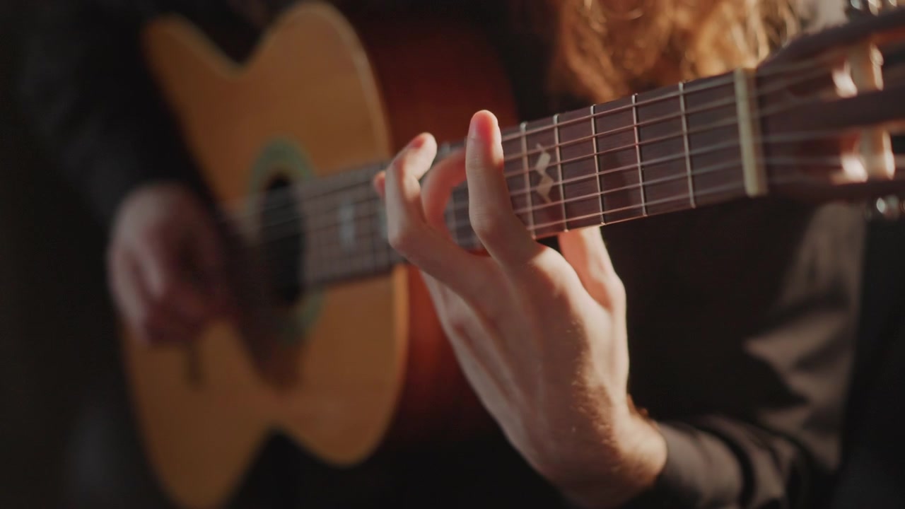 Primo piano della mano sinistra che preme le corde sulla tastiera in stile fingerstyle, chitarrista dai capelli lunghi che pratica scale e arpeggi sotto una luce calda e soffusa, mano destra che pizzica, attenzione tecnica, guida del tutor, prova intima