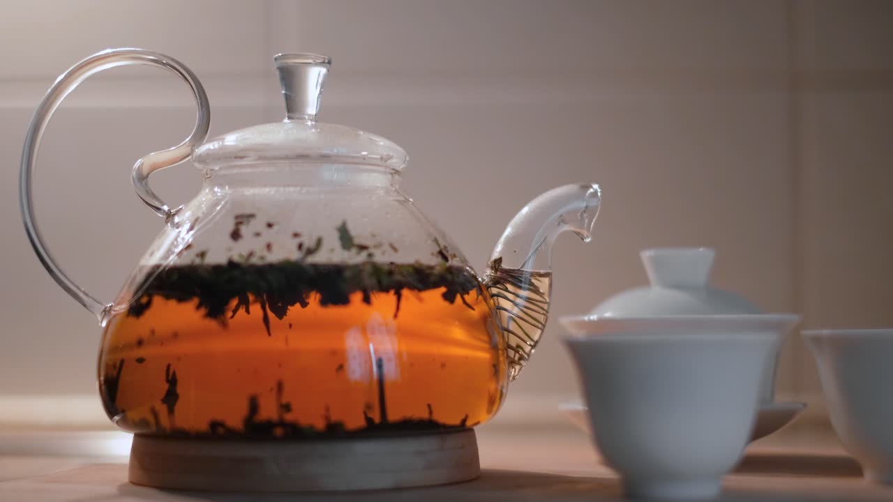 tetera de vidrio con hojas de té y tazas de té
