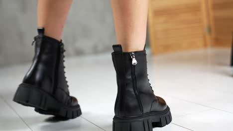 female wearing the black low autumn boots with laces. model turning in front of camera showing stylish footwear. close up. white backdrop.