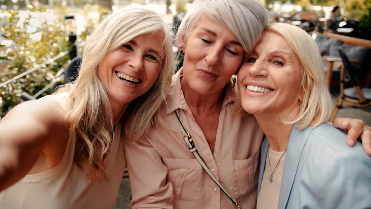 Elegant senior women having fun taking selfies together at cafe