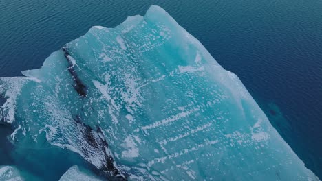 Aerial-view-over-an-iceberg-in-the-glacial-water-of-Jokulsarlón-lake,-in-Iceland,-during-winter