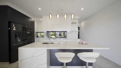 modern luxurious contemporary kitchen white marble bench top drop lighting marble tiled floors breakfast bench seating, black feature wall with sleek black appliances fridge white kitchen storage