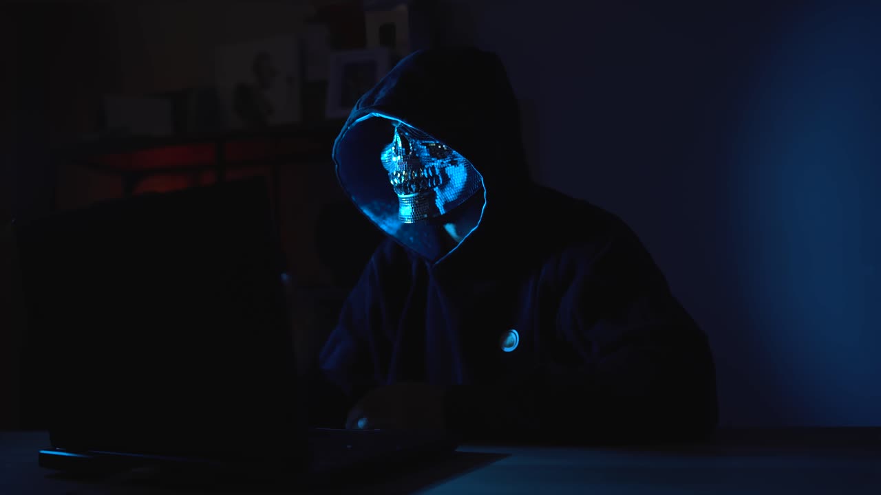 Hacker in Hoodie and Face Mask Hiding in Shadows While Typing – Symbol of Blackmarket Intrusion, Cyber Attacks, and Digital Theft