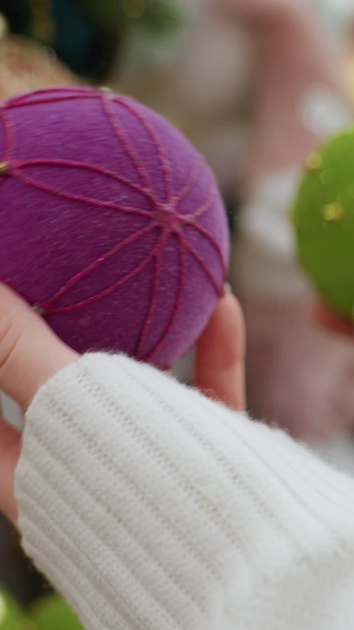 Close up hand view of young lady playfully jamming green and purple decorative balls together while shopping for Christmas ornaments in a festive store
