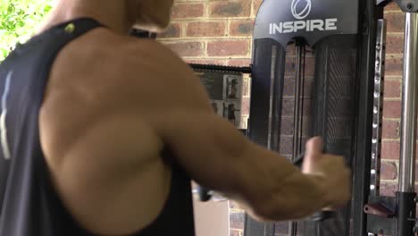hombre musculoso en el gimnasio en casa haciendo ejercicio de un solo brazo con cable swing