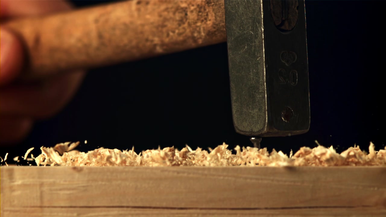 Zeitlupen-Nahaufnahme eines Hammers, der eine Schraube in Holz treibt