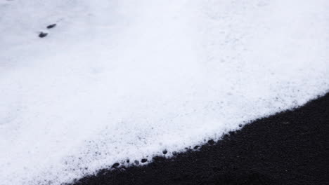 Wunderschöne-Aufnahme-Von-Schäumenden-Wellen,-Die-Sich-über-Den-Schwarzen-Sandstrand-Von-Reynisfjara-In-Island-Bewegen