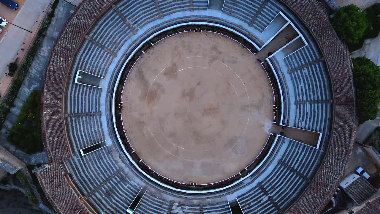Drone shot rising vertically over an empty bullring arena in Brihuega, Spain, revealing the full circular architecture from a close-up sand view to a wide aerial perspective