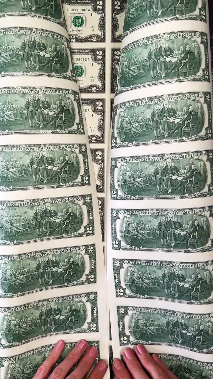 Foglio di dollari souvenir con mani. Mani che tengono un grande foglio di banconote souvenir da due dollari durante il processo di stampa.