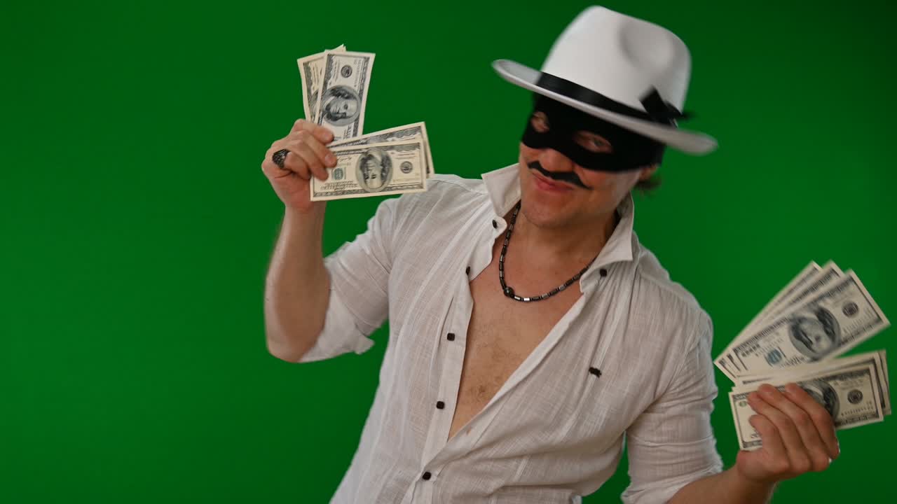 검은 마스크와  모자를 입은 매력적인 사기은 녹색 배경에서 돈을 즐기고 유혹합니다.