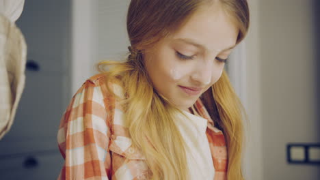 Close-up-of-the-cute-blonde-girl-making-forms-with-a-daugh-and-smiling-next-to-her-mother-in-the-kitchen.-Portrait-shot.-Inside