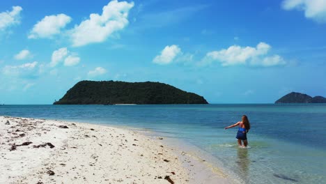 Girl-washing-her-feet-on-calm-fresh-water-of-shallow-sea-lagoon,-exotic-beach-with-beautiful-tropical-islands-background,-Koh-Pha-Ngan,-Thailand