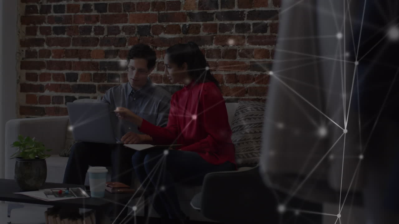 Animation of network of connections over male and female colleague using laptop on couch in office
