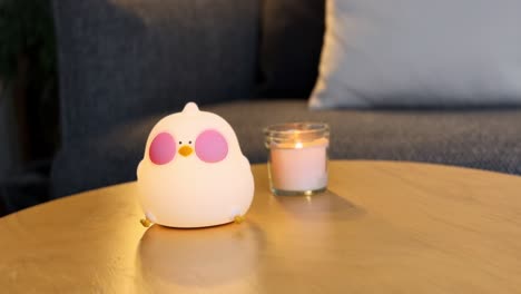 hand waving over an adorable bird-shaped night lamp on a cozy table beside a lit candle. perfect for themes of cuteness, ambiance, and nighttime relaxation or bedtime rituals.