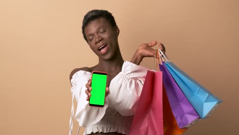 transgender person with shopping bags showing a mobile blank screen over beige background