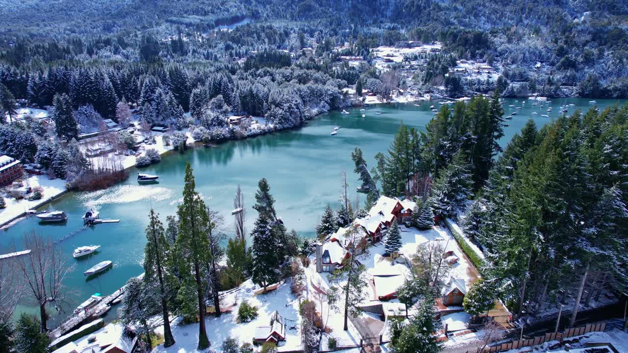 Drone che sale verticalmente mentre la telecamera si inclina verso il basso, passando da una vista panoramica delle Ande a un'inquadratura dall'alto di una baia innevata con barche sul lago Nahuel Huapi in Patagonia
