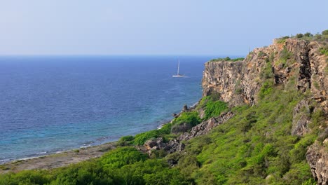 Drone-dolly-past-Caribbean-cliff-as-Catamaran-sails-in-open-clear-blue-water