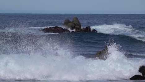 incoming waves break violently on shore rocks, splashing up sea foam