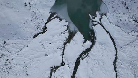 Top-down-drone-view-of-the-delta-of-a-frozen-glacier-river-in-the-Alps-from-a-Drone-in-Winter-on-a-sunny-day,-Italy