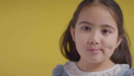 studio portrait of shy young girl smiling and laughing against yellow background 1