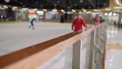 a blurry view of a skiing area featuring a person in a red sleeve shirt and other people skiing, this video highlights the dynamic environment and polished handrail in the foreground