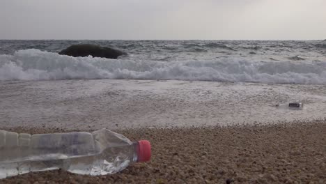 littered plastic drinking bottle left on a beach near waves, steady low angle shot