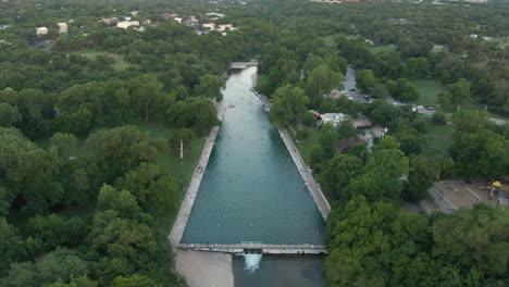 aerial pan around barton springs pool in austin, texas at dawn with many people swimming at once.