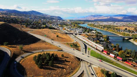 normal speed dolly in drone shot of kamloops bc canada with bridges, the highway 1 and yellowhead highway 5 on a sunny day in the desert city with cars,semi trucks and trains driving in the foreground