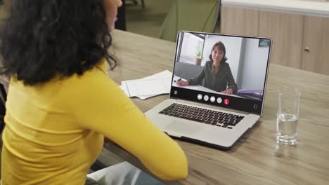 biracial woman using laptop for video call, with business colleague on screen