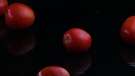 tomates de cereza rodando en un charco de agua negra y volando hacia arriba fuera del marco