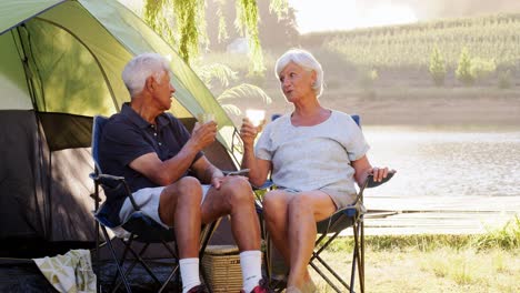una pareja de mayores en vacaciones de camping sentados junto a la tienda hablando