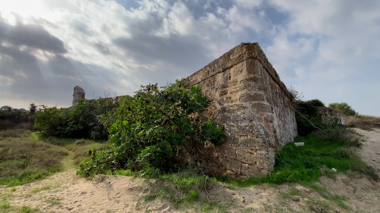Las paredes de piedra iluminadas por el sol del castillo de Sanlúcar se elevan sobre los arbustos en flor y una solitaria farola, mezclando la arquitectura medieval con exuberantes jardines.