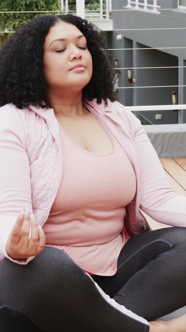 Video verticale: Donna che pratica esercizi di respirazione su una terrazza panoramica, indossa un top rosa e leggings scuri.