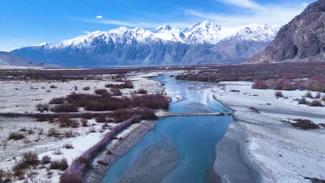 aerial drone shot showcasing the clear blue waters of a river flowing through a remote ladakhi valley, contrasting with the arid surroundings.