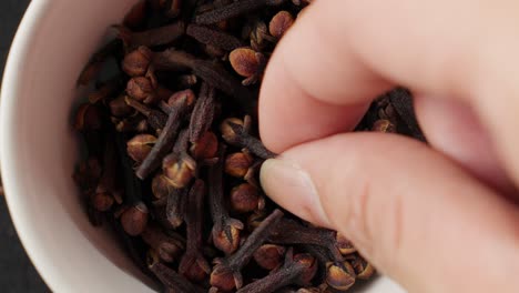 hand picking dried cloves from a white bowl, capturing the aromatic spices up close