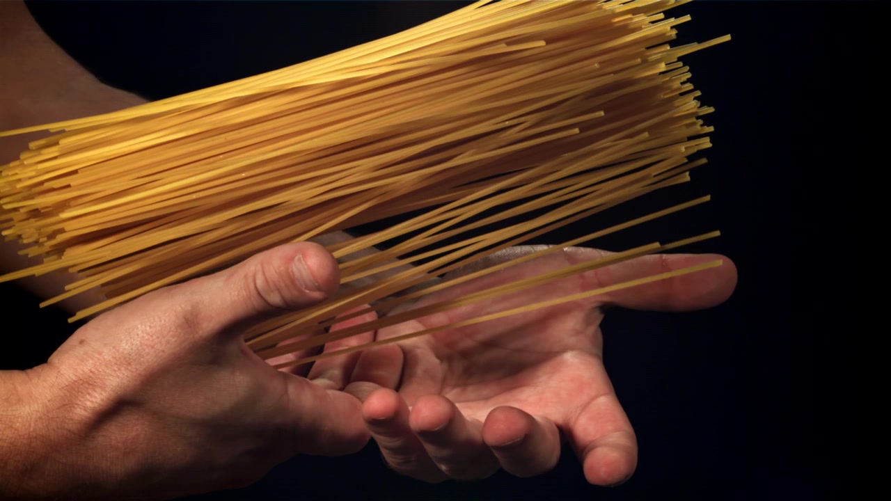 Primo piano di mani che tengono e lasciano cadere spaghetti crudi