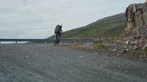 Cyclist-on-E-bike-Passes-Through-The-Curve-Dirt-Road-Of-Norway