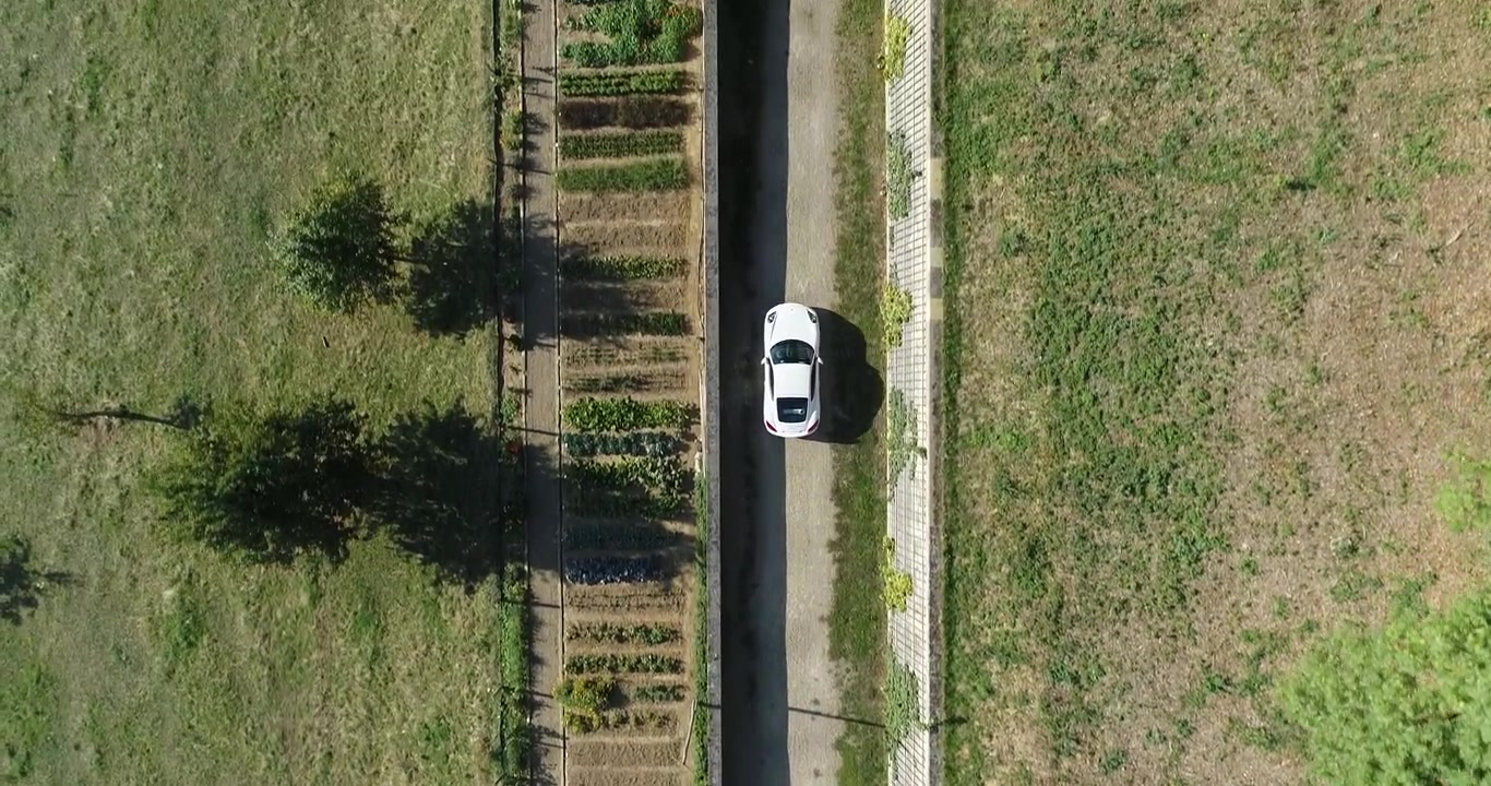 Ripresa aerea dall'alto di una Porsche bianca che guida su una strada di campagna all'alba.