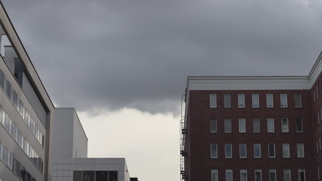 Timelapse of dramatic dark clouds rolling over modern office buildings in a cityscape