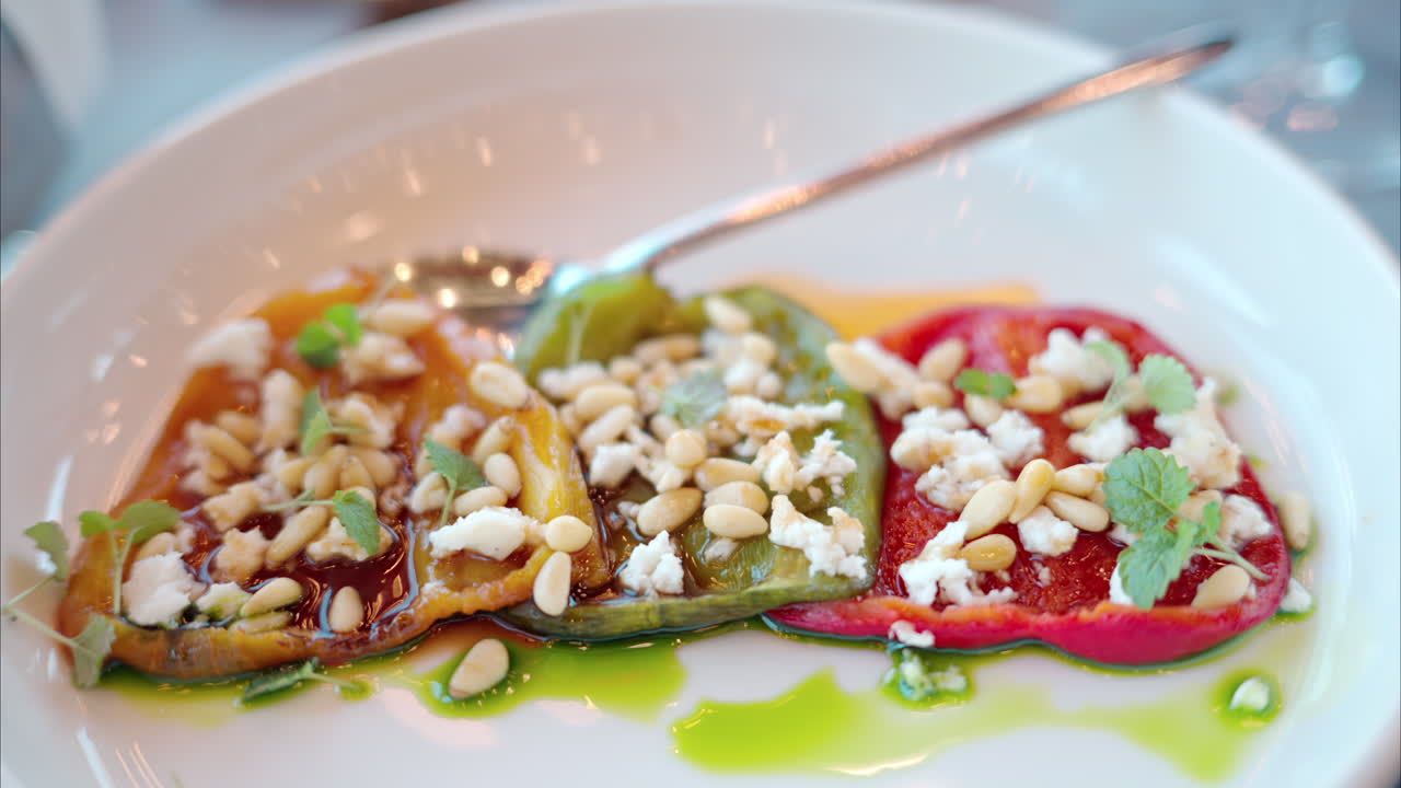 Close-up of three, multicoloured bell peppers with pine nuts and feta cheese served on a white plate